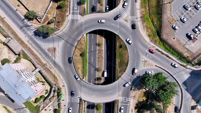 Top down ascending aerial shot over circular urban roundabout with cars flowing around the ring road intersection and surrounding streets revealing the geometric traffic pattern
