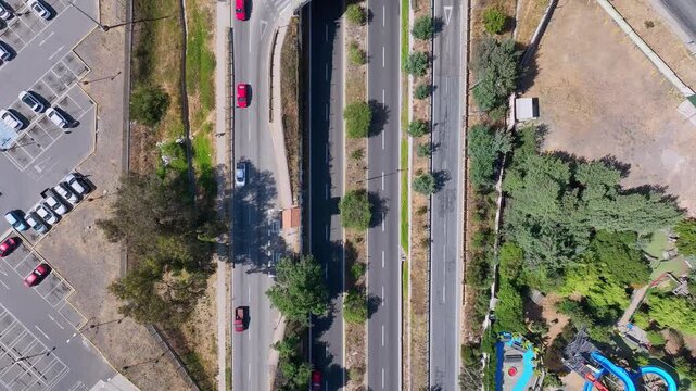 Bird's eye view over urban roundabout overpass with cars and bus flowing through circular ring road above highway underpass with parking lot and green verges visible below