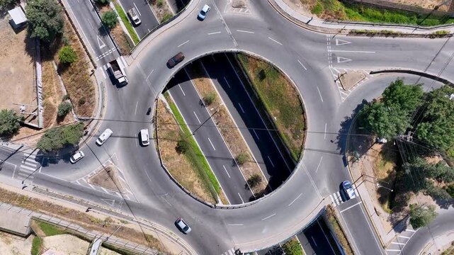 Ascending spiral aerial shot directly above urban roundabout with cars and trucks flowing around circular ring road intersection revealing the perfect geometric traffic pattern