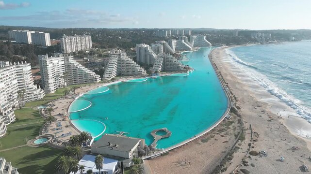 Pull back flight over San Alfonso del Mar revealing the full extent of the worlds largest turquoise pool flanked by resort towers and Pacific Ocean beach. Algarrobo, Chile