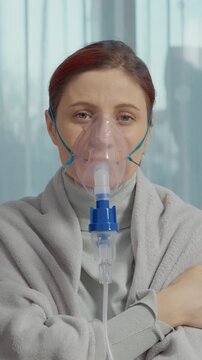 Vertical Screen: A woman sits in a room wearing a mask connected to a nebulizer. She inhales steam from a saline solution to help with respiratory issues like coughs and allergies.