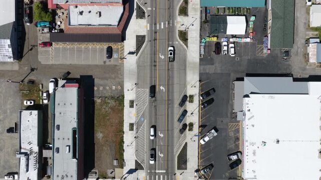 Top-down view of urban intersection with crosswalks, turn arrows, parked vehicles and commercial rooftops casting sharp shadows on sunny day. Washington State. Aerial view. Flyover. Rooftops of houses