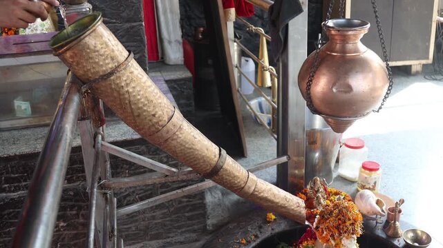 Raw video footage of devotees pouring holy water through a brass pipe inside a Hindu temple in Uttarakhand India during traditional worship and prayer ritual.