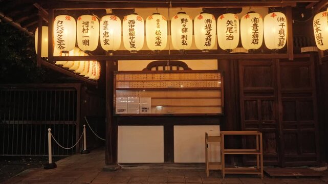 A row of glowing chochin paper lanterns lights the front facade of a traditional Kyoto shrine building at night.