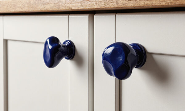 Ceramic knobs hardware deep blue artisanal door pulls installed on white kitchen cabinets for a modern interior design