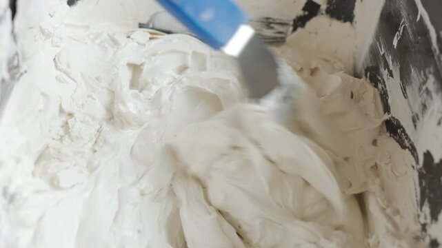 Artist mixes white plaster paste in a container with a palette knife. Concept of textured artwork, DIY wall decor and creative hobby.