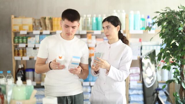 Man chooses skin cream in modern pharmacy. Female pharmacist helps with choosing a medicine. High quality 4k footage
