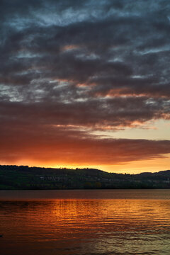 Dramatic sunset over a lake with glowing reflection and layered clouds above rolling hills