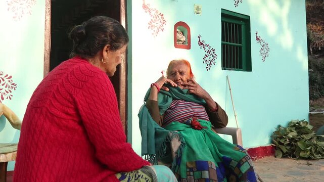 Raw video footage of elderly rural Indian women sitting and talking outside a traditional village home in Uttarakhand India showcasing countryside lifestyle and daily life.