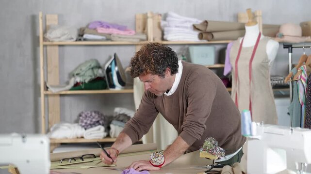 Adult male tailor drawing pattern on paper in sewing workshop
