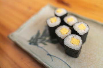 Six pieces of tamago maki sushi on a decorative plate. © bonnontawat