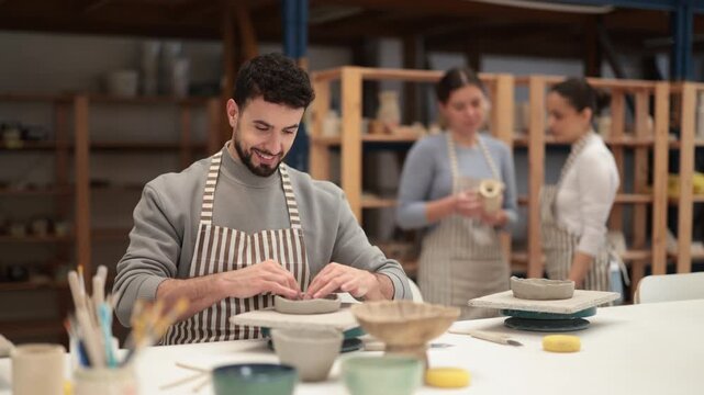 In pottery workshop, guy sitting at table, busy making products from raw clay. Amateur busy at master class modeling clay plates from clay