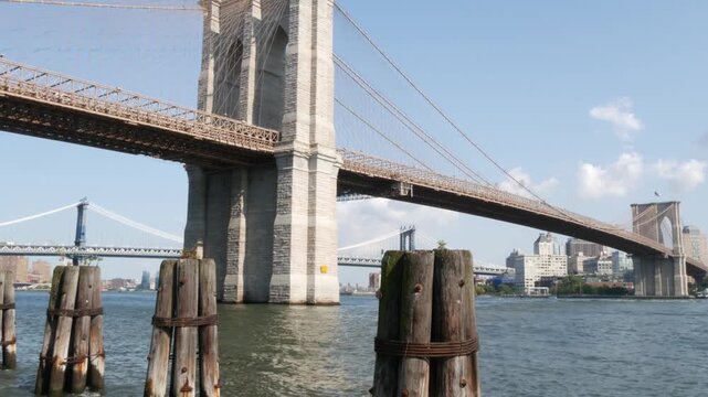 Brooklyn Bridge and Manhattan Bridge from Downtown, New York City, United States. Esplanade park. American architecture, famous tourist landmark. Waterfront urban promenade. Old wooden pier piles