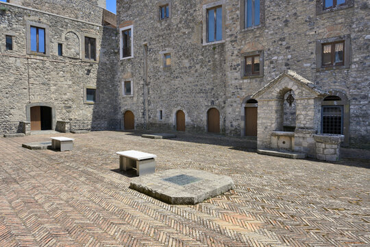 Melfi Castle courtyard showing historic medieval architecture and well. Historic Melfi Castle interior courtyard with stone walls, arched doorways, paved floor, and ancient well.