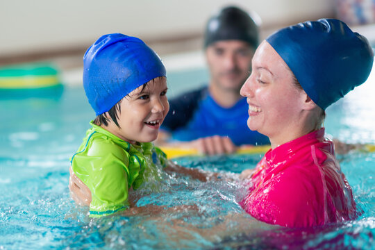 Swim instructor supports a smiling toddler during an aquatic lesson in an indoor pool, building water confidence and early motor skill development.