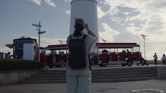 This outdoor paved square features sightseeing shuttle trains stopped on a raised stairway, with several passengers waiting or riding the vehicles under soft daytime light.