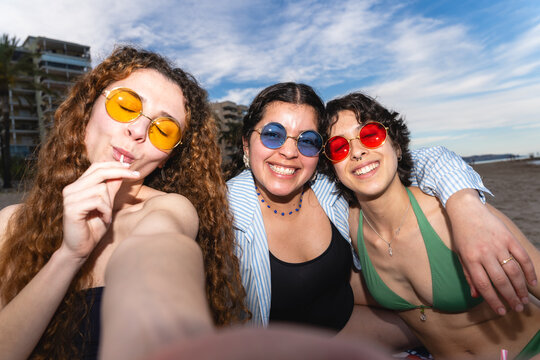 Three young women smiling, taking a selfie, and having fun at the beach
