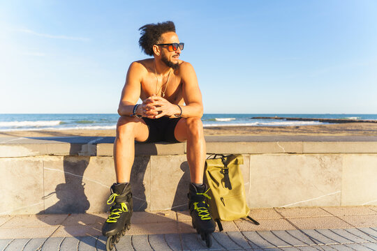 Man with rollerblades sitting on a wall, enjoying the coastal view and sunny weather