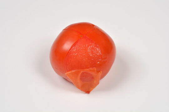 A whole ripe red tomato scored with a cross at the top and partially peeled after blanching isolated on a white surface