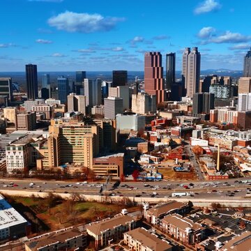 Cinematic aerial view of downtown Atlanta skyline featuring modern skyscrapers and busy highway traffic under blue sky.