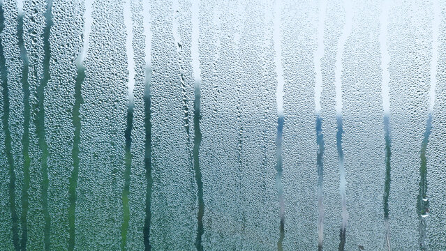 Condensing water drops creating a wet texture on a glass window surface