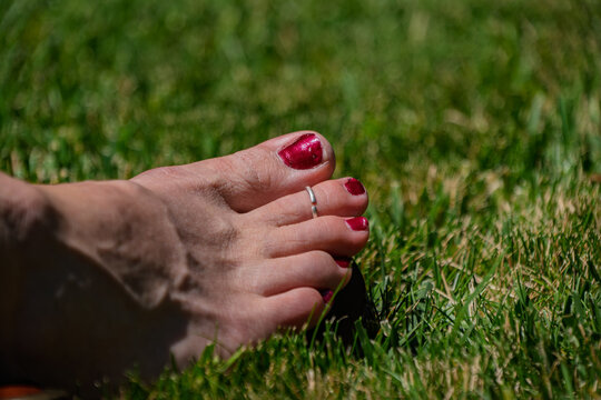 Foot with painted toenails and a silver toe ring on grass