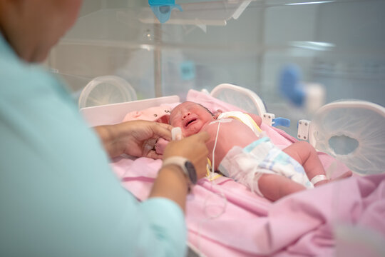 Nurse Caring for Crying Newborn Baby Inside Hospital Incubator