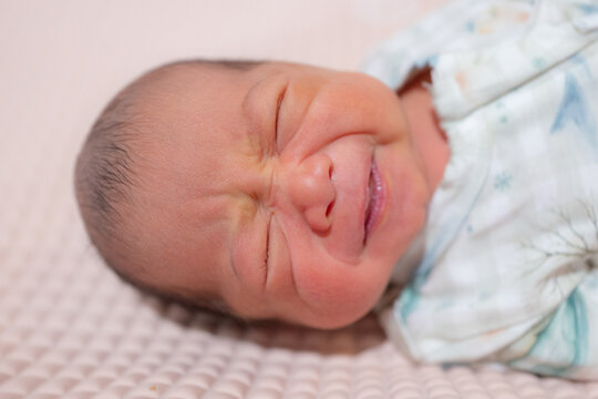 Close-up of a Cute Newborn Baby Making a Funny Crying or Grimacing Face While Sleeping on a Textured Blanket