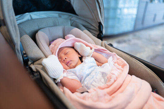 Cute Newborn Baby Girl Sleeping Peacefully in a Car Seat Bassinet Stroller with Pink Blanket