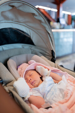 Vertical Close-up of a Cute Newborn Baby Sleeping in a Car Seat Bassinet Stroller with Pink Blanket