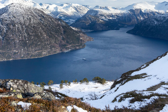 A beautiful winter day landscape from the Blahornet mountain towards fjord with a ferry crossing. A scenery in the Eidsdal hiking area, Geiranger Unesco World Heritage Site, Sunnmore region, Norway.