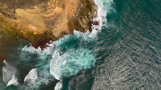 Vertical aerial ekas view looks down on rocky cliff edge as powerful surf explodes into white foam creating dramatic ocean nature texture and coastal geology imagery