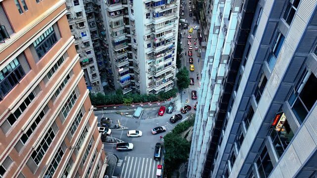 Static high-angle wide shot looking down at vehicles navigating a curved narrow street between dense residential towers in Chongqing; congested and cinematic urban atmosphere view from Kuixing Tower