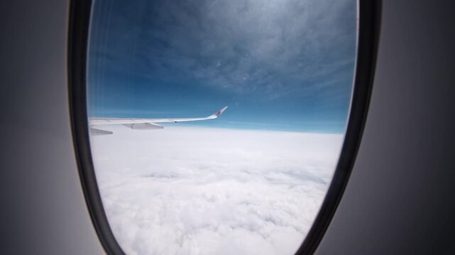 An airplane wingtip extends into a sky filled with clouds, captured through a window. Ideal for aviation themes or travel content.