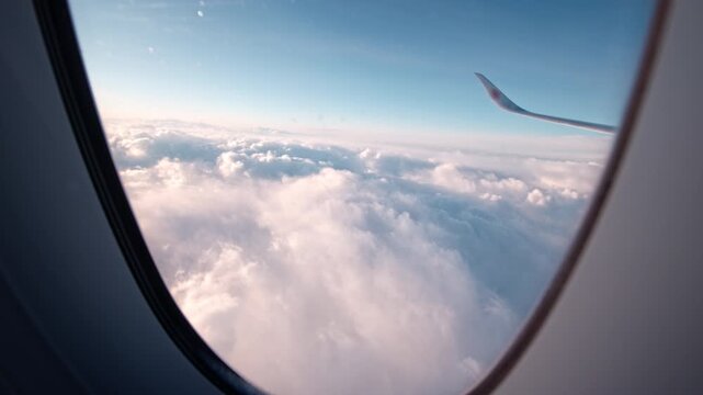 Soft clouds float below an airplane wing, captured from a window seat. Ideal for travel content or aviation-themed projects.