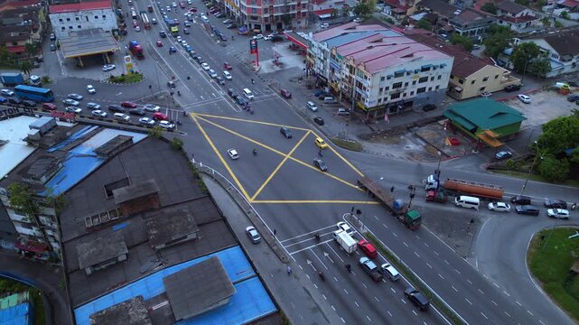 cars, trucks, and motorcycles navigating a busy diamond intersection in a Malaysian urban area. Dramatic aerial view drone camera pointing down
