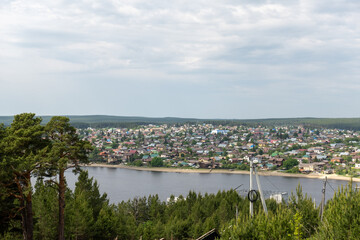 Naklejka premium Panoramic view of a riverside town nestled amongst lush green trees under a cloudy sky