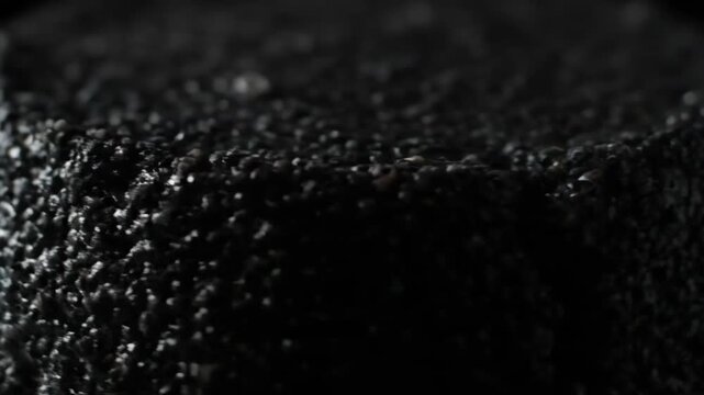 Macro shot of deep dark black rough textured surface, suggesting gourmet chocolate cake or a cocoa covered confectionery coating with granular detail in dramatic low key lighting.