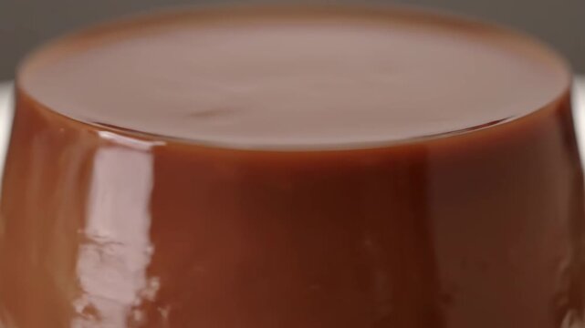 Extreme close-up of glossy chocolate pudding or caramel flan dessert showing smooth, reflective surface and perfect texture