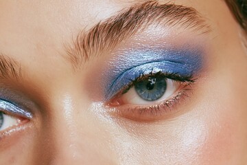 Fototapeta premium Close up of a woman's eyes and upper face showcasing vibrant blue eyeshadow and natural skin texture, emphasizing makeup artistry and beauty trends