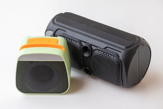 A small lime-green mini speaker next to a tall black outdoor multimedia soundbox. Perfect concept for consumer electronics product reviews, mobile audio technology, and youthful lifestyle accessories.