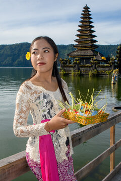 Balinese woman in white lace kebaya holding ceremonial offering tray with incense at Pura Ulun Danu Batur temple