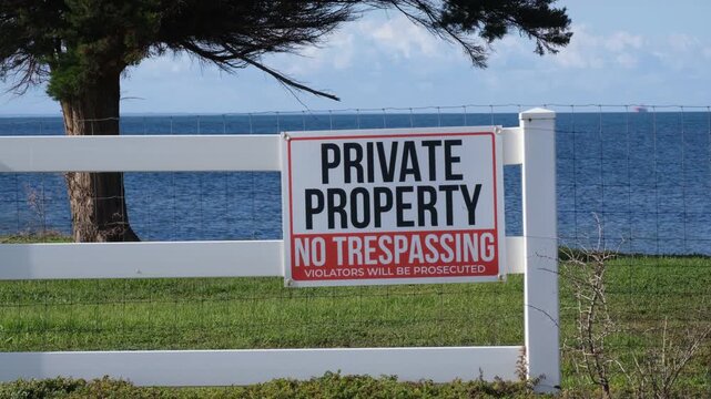 Warning sign reading "Private Property, No Trespassing, Violators Will Be Prosecuted" is on boundary fence of a rural property by the sea in Australia. Legal ownership, security, and restricted access