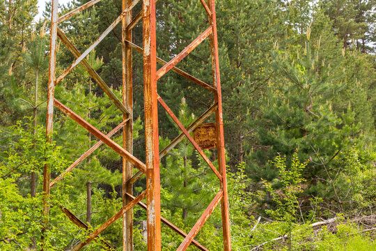 old rusty metal utility tower standing in a lush green pine forest, representing the concept of technology decay, human impact on nature, environmental abandonment