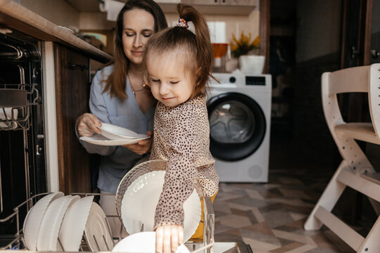 Mother and daughter unloading dishwasher together in kitchen