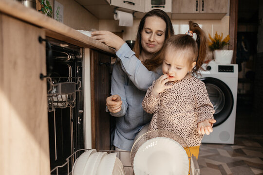 Mother and daughter unloading dishwasher together in kitchen