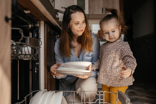 Mother and daughter unloading dishwasher together in kitchen