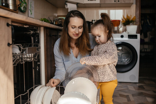 Mother and daughter unloading dishwasher together in kitchen