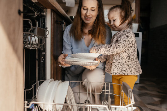 Mother and daughter unloading dishwasher together in kitchen