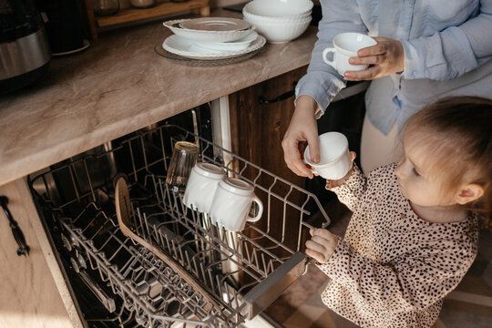 Mother and daughter unloading clean dishes in the kitchen